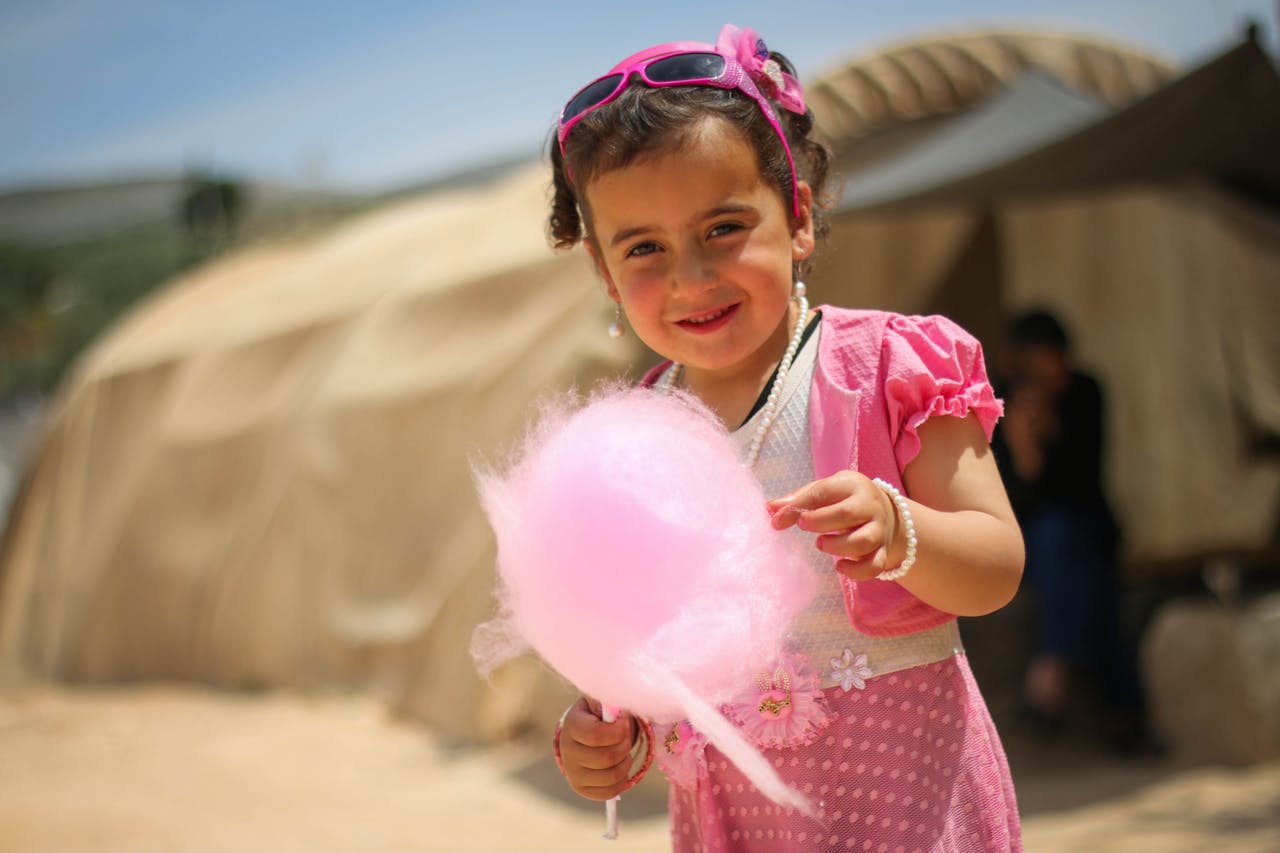Happy little girl enjoying pink cotton candy outside a tent in Idlib, Syria.